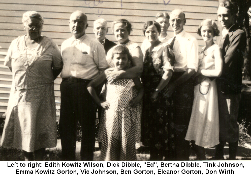 Sepia-tone photo of Edith Kowitz Wilson, Richard 'Dick' Dibble, 'Ed', Bertha Kowitz Dibble, Shirley 'Tink' Johnson, Emma Kowitz Gorton, Victor Johnson, Ben Gorton, Eleanor Gorton, and Don Wirth, standing before a frame house wall.